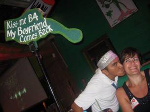 Jeff being kissed by a waiter under a sign reading 'Kiss me B4 my boyfriend comes back'